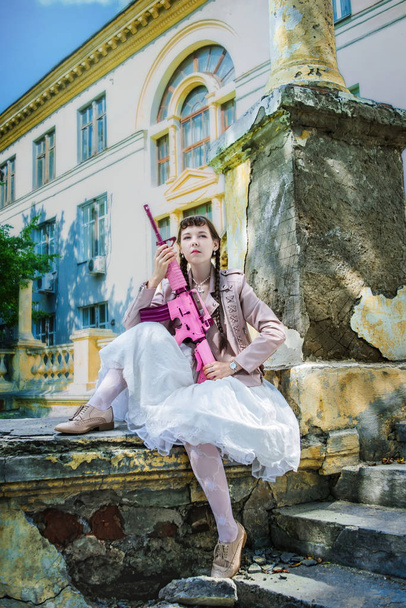 Girl in a white dress with a pink rifle plays airsoft - Zdjęcie, obraz