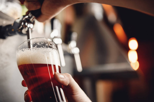 Barman derrama cerveja bebida artesanal de torneira em vidro, fundo escuro
 - Foto, Imagem