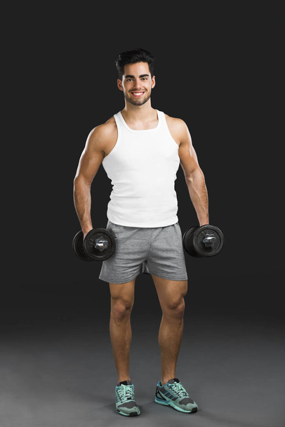 Portrait of handsome young man lifting weights, isolated over a gray background - Foto, Imagem