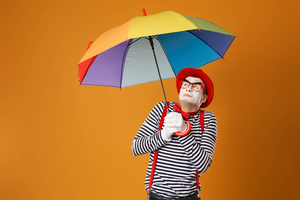 Mime with multi-colored umbrella on empty orange background - Photo, image