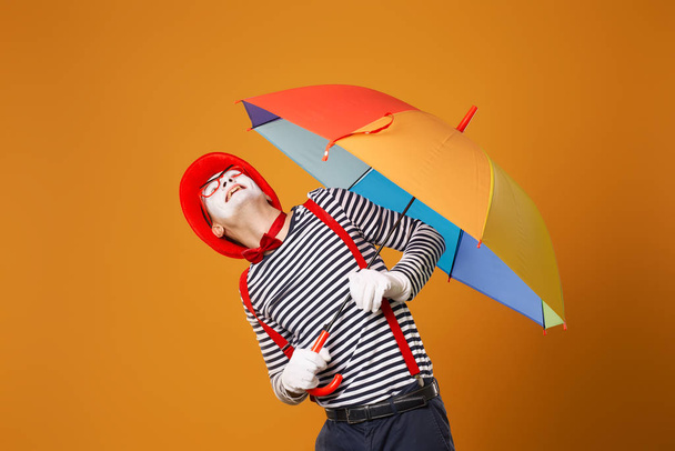 MIME muž vzhlíží s multi-barevný deštník v ruce izolované na prázdném oranžovém pozadí - Fotografie, Obrázek