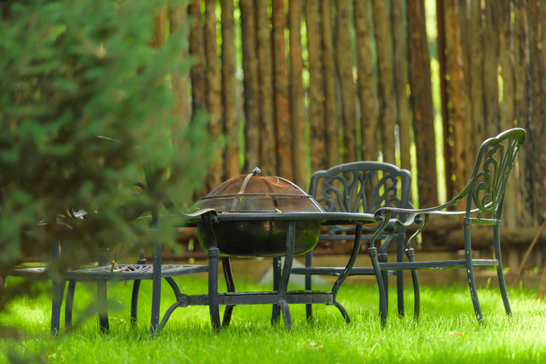 Садові меблі з вбудованим каміном вогнища барбекю на столі. Зона відпочинку з вогнищем барбекю. Металеві садові стільці та стіл. Садовий стіл з каміном
 - Фото, зображення