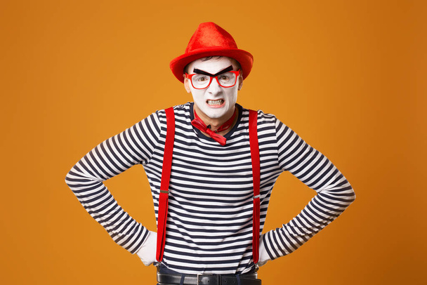 Young mime in white gloves and red hat on orange background - Foto, Imagen