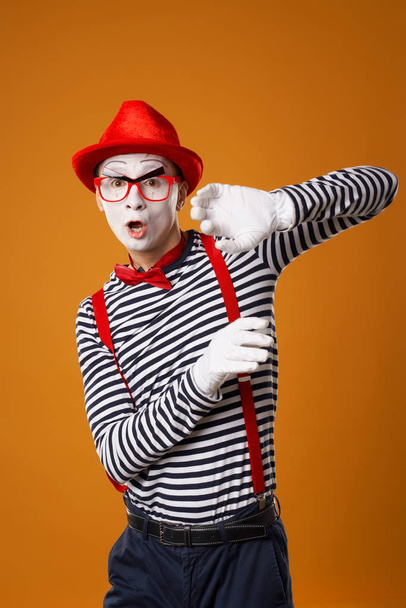 Serious young mime in white gloves and red hat looking at camera on orange background - Photo, image