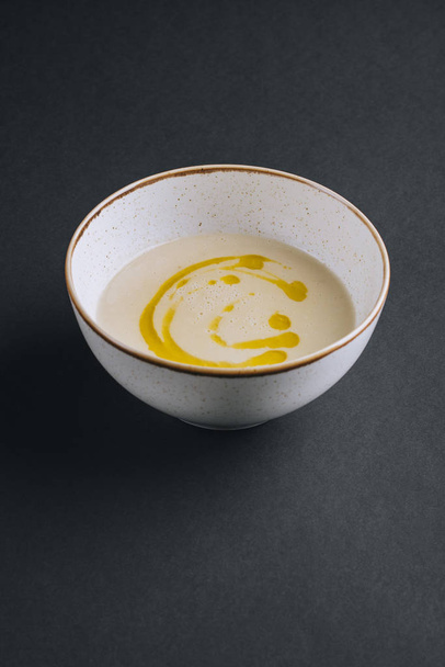 Peruna kerma keitto oliiviöljyn valkoinen levy mustalla pohjalla
 - Valokuva, kuva