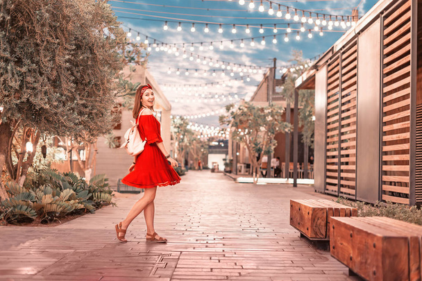 Kırmızı elbiseli mutlu kız tatil köyünde modern bölgede yürüyor, seyahat ve tatil konsepti. - Fotoğraf, Görsel