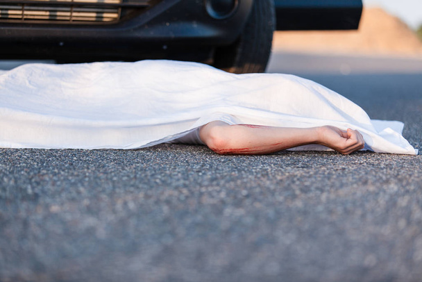 Body of a young child covered by a sheet lying on the street in front of the bumper of the car that ran him over with foreground copyspace - Fotoğraf, Görsel
