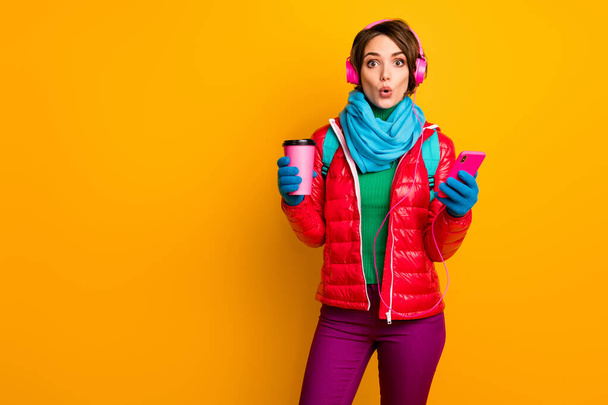 Photo of funny blogger lady open mouth hold telephone listen earphones youth music drink coffee wear casual red coat blue scarf gloves pants isolated yellow color background - Photo, image
