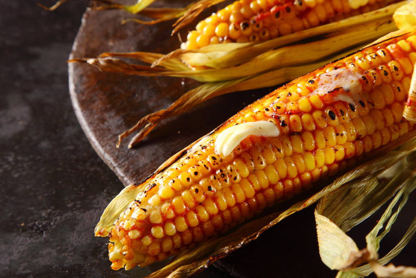 Grilled or roasted fresh corn, maize or mealies on the cob served with a dollop of melted butter for a delicious autumn snack - Foto, afbeelding