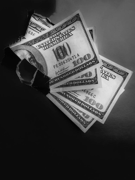 Dollars met Benjamin Franklin biljet in een gescheurd gat in zwart papier. Het concept van verborgen inkomstenbelasting ontduiking, donatie, winst, corruptie, armoede, voordelen, beurzen, en vrijgevigheid Kopieer ruimte - Foto, afbeelding