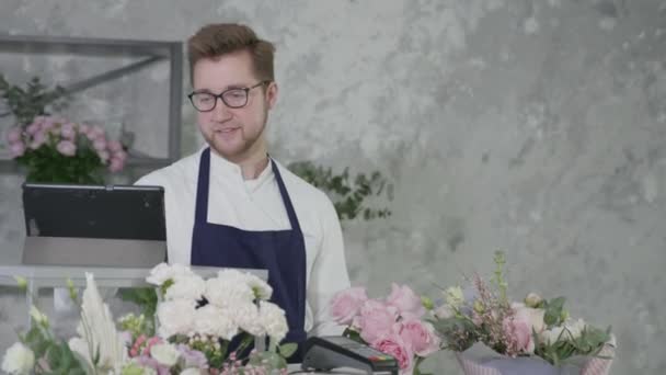 flower boutique, smiling man representative of gender equality sells beautiful bouquet of flowers to charming buyer, contactless payment - Footage, Video