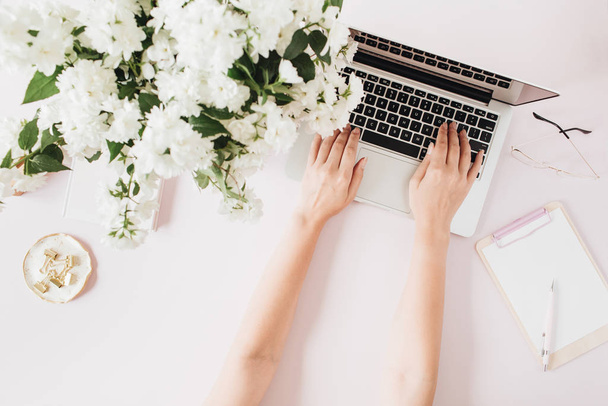 Woman work on laptop. Office desk workspace with computer, flowers bouquet and stationery on pink table. Flat lay, top view work / business hero header background. - 写真・画像
