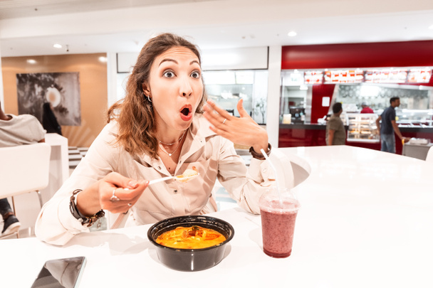 A woman eating too hot and peppery soup in an Asian fast food restaurant. Concept of spices in Oriental cuisine - Photo, Image