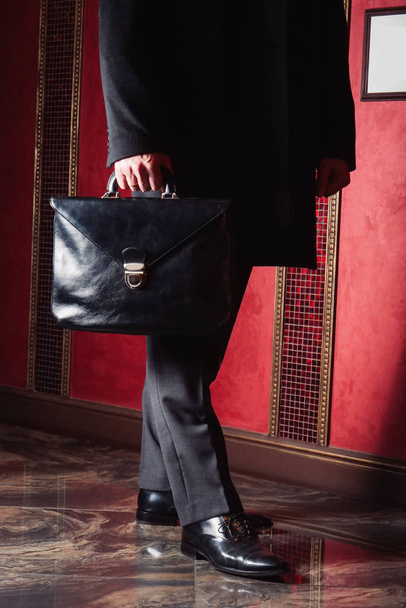 a man in a business suit and long coat with a black leather briefcase in a business center - Foto, imagen