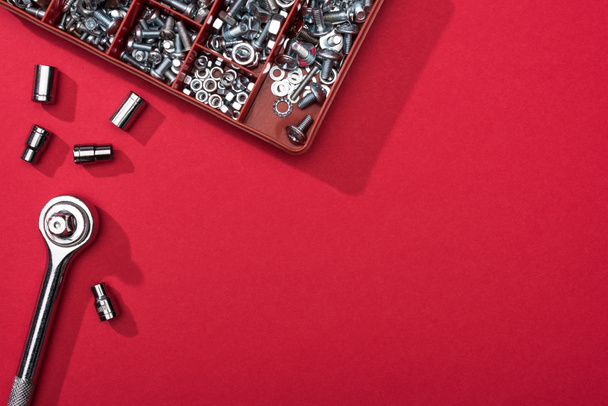 Vista superior de la llave inglesa con boquillas y caja de herramientas con pernos y tuercas sobre fondo rojo
 - Foto, Imagen