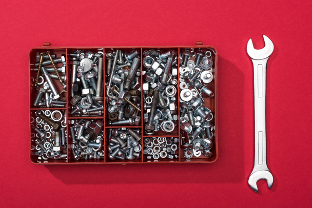 Top view of toolbox with nuts and bolts near wrench on red background - Fotografie, Obrázek