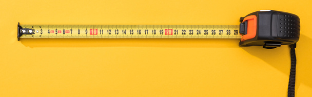 Vista superior de cinta métrica industrial sobre fondo amarillo, plano panorámico
 - Foto, Imagen