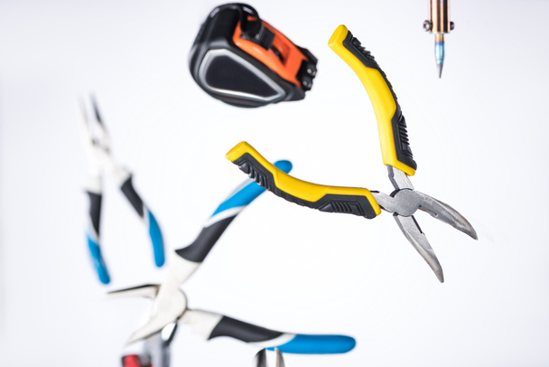 Selective focus of pliers, soldering iron and measuring tape levitating in air isolated on white - Foto, afbeelding