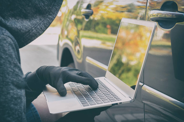 Hooded thief tries to break the car's security systems with lapt - Zdjęcie, obraz