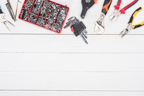 Vista superior de la caja de herramientas con alicates y llave inglesa sobre fondo de madera blanco
 - Foto, Imagen