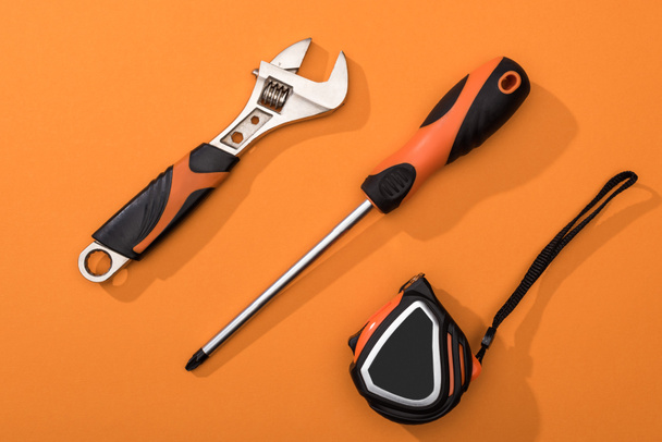 Top view of wrench, screwdriver and measuring tape on orange background - Foto, imagen