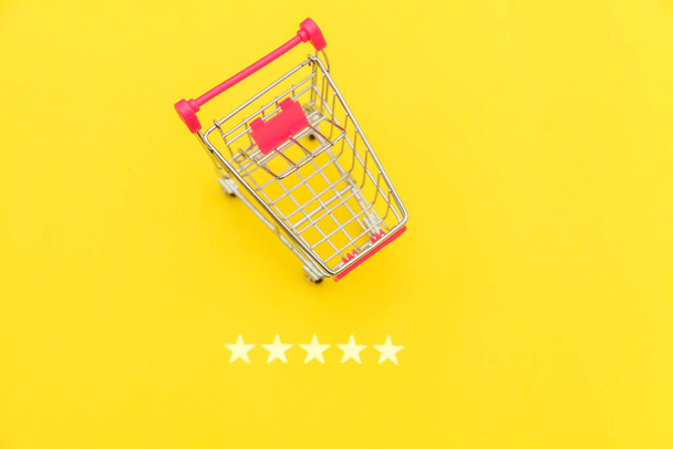 Pequeño supermercado carrito de compras empuje para juguete de compras con ruedas y clasificación de 5 estrellas aislado sobre fondo amarillo. Compras al por menor concepto de evaluación y revisión en línea
. - Foto, imagen