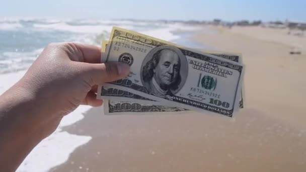 Mädchen hält Geldschein in Höhe von 300 Dollar vor dem Hintergrund der Meereswellen - Filmmaterial, Video