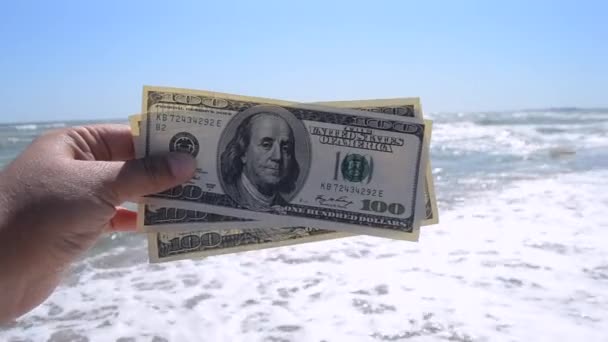 Chica sosteniendo la factura de dinero de 300 dólares en el fondo de las olas del mar
 - Imágenes, Vídeo