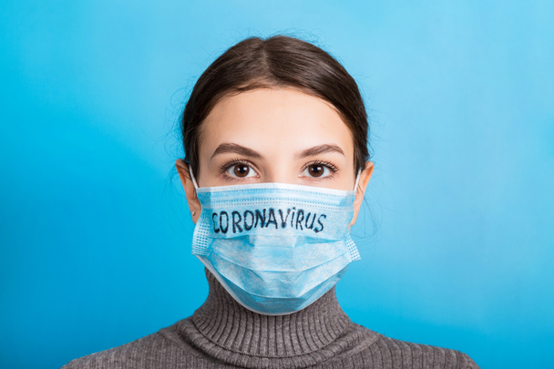 青の背景にコロナウイルスのテキストを持つ医療用マスクの女性の肖像画。コロナウイルスの概念。呼吸器保護 - 写真・画像