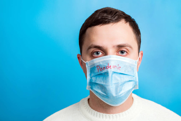 Portrait of young man in protective mask with pandemic text at blue background. Coronavirus and health care concept - Foto, Bild