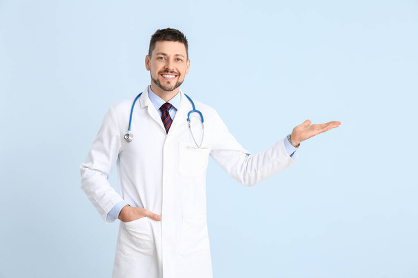 Portrait of male doctor showing something on color background - 写真・画像