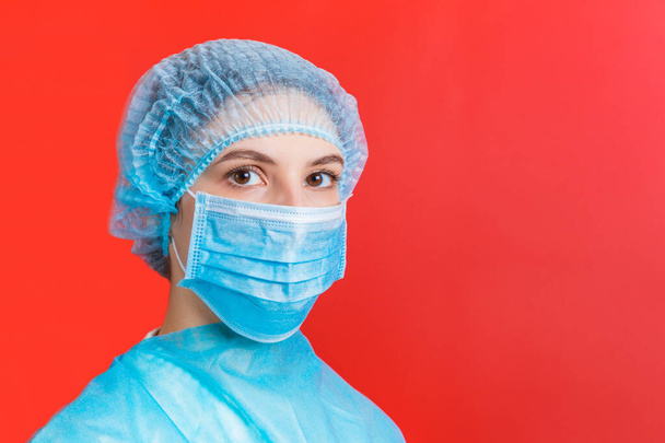 Egy orvosi egyenruhát és maszkot viselő nő portréja a vörös háttérben. Coronavirus koncepció. Védje az egészségügyi koncepció másolási hely - Fotó, kép