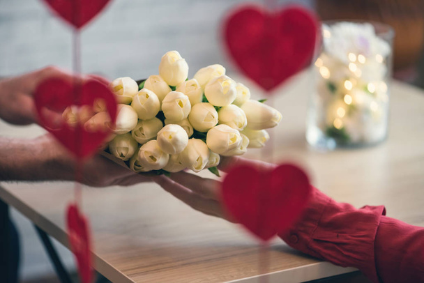 Valentines day.  Close-up of woman and man celebrating in restaurant. Boyfriend giving bouquet of flowers tulips to girlfriend. View through a heart-shaped garland. love, romance, date - 写真・画像