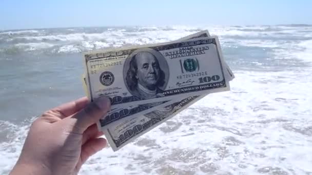 Девушка с купюрой в 300 долларов на фоне морских волн - Кадры, видео