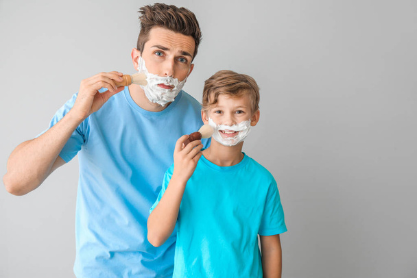 Father with son applying shaving foam onto their faces against light background - Photo, Image