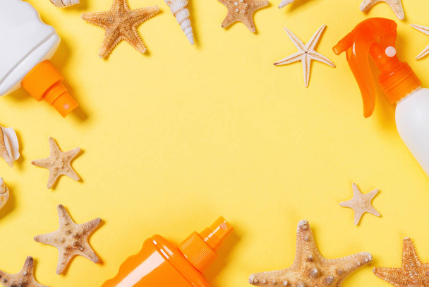 sunscreen cream with starfish and seashells in bottles on yellow background, top view - 写真・画像