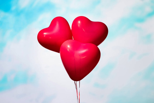man and woman hands holding three reds balloons in form of heart on the sky background in the blue pastel color. The concept of Valentines day. - Photo, Image