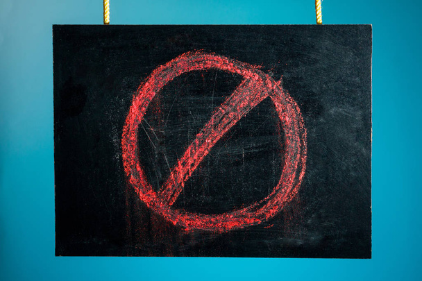 La pizarra de tiza está suspendida con un patrón de una señal de prohibición roja sobre un fondo azul. espacio de copia
 - Foto, Imagen