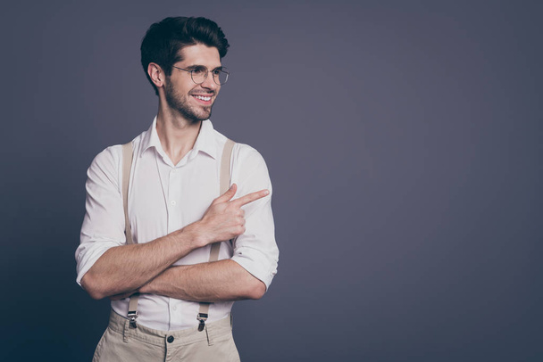 Photo of attractive business man charming appearance indicating finger looking empty space dressed formalwear white shirt beige suspenders specs isolated grey color background - Foto, immagini