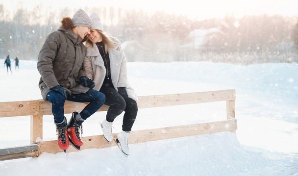 Winter outdoor activities. Loving couple girl and young man ice skating rink, in background sunlight - 写真・画像