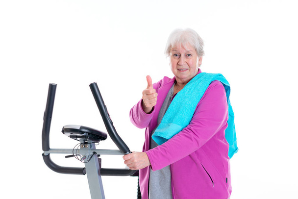 gray-haired female senior with thumb up train with fitness machine - Φωτογραφία, εικόνα