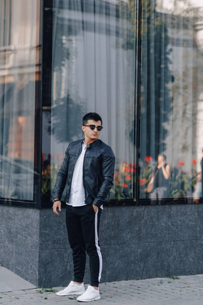 young stylish guy in glasses in black leather jacket on glass background - 写真・画像