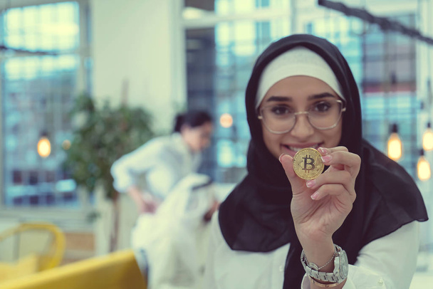 Young arabian muslim woman in hijab black clothes hold in hand holding bitcoin. Cryptocurrency exchange - Фото, изображение
