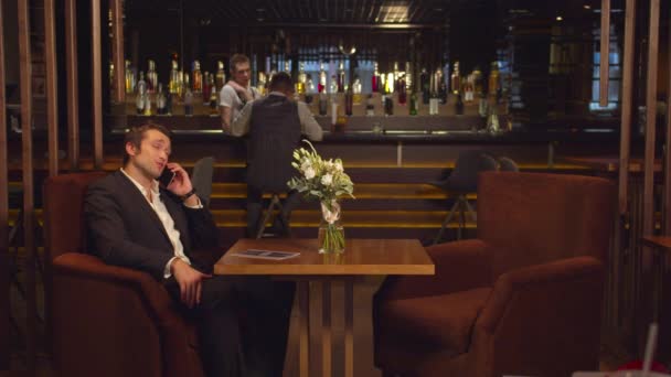 Homem se senta em uma mesa em um café e fala ao telefone
  - Filmagem, Vídeo