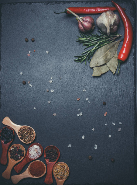 Spices in wooden spoons and cherry tomatoes, chili peppers, garlic and herbs for cooking on a black surface and black background - Φωτογραφία, εικόνα