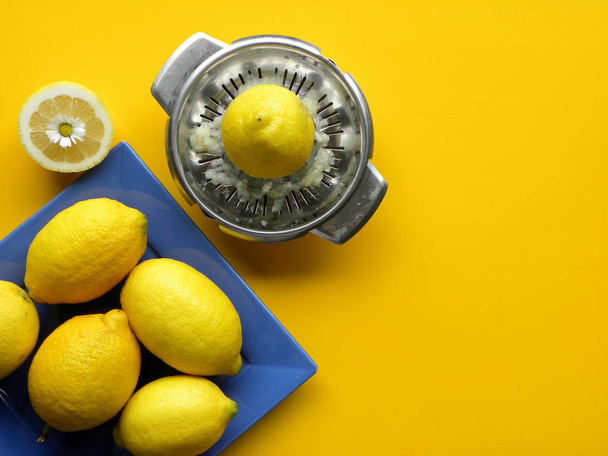         ώριμα λεμόνια σε μπλε πιάτο και ένας χειρωνακτικός αποχυμωτής χάλυβα σε κίτρινο φόντο                        - Φωτογραφία, εικόνα