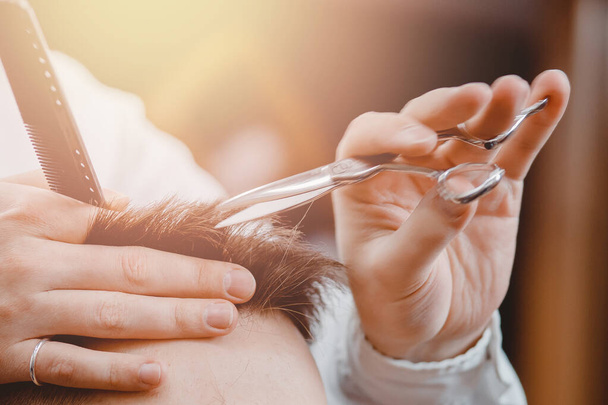 Close up of male hairdresser cutting hair with scissors, brown tinting, barber shop concept - Photo, Image