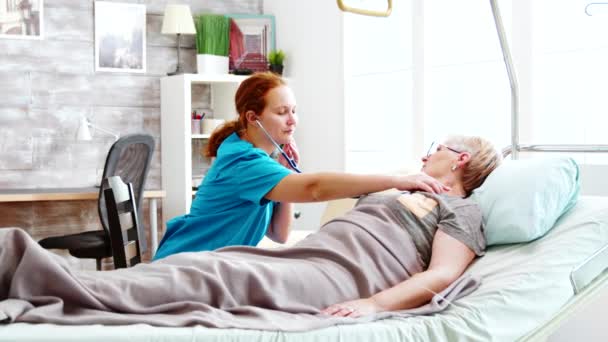 Kafkas kadın hemşire hastane yatağında yatan yaşlı bir kadının kalp atışlarını ölçüyor. - Video, Çekim