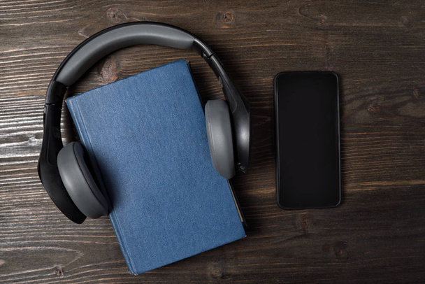 Mobiltelefon és könyv fülhallgatóval fából készült háttérrel. Audiobook koncepció. Felülnézet, másolás. - Fotó, kép