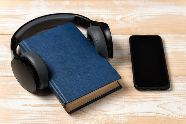 Headphones, phone and book. Learning through Audiobook concept. Wooden background - Foto, afbeelding
